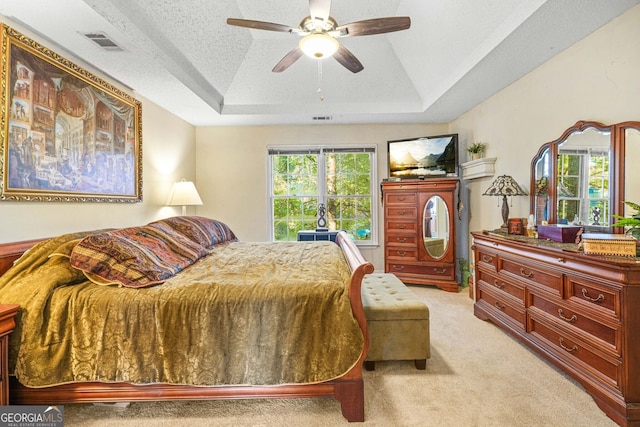 carpeted bedroom with ceiling fan, a tray ceiling, and a textured ceiling