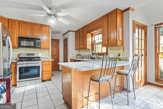 kitchen with light tile patterned flooring, a textured ceiling, appliances with stainless steel finishes, a kitchen breakfast bar, and kitchen peninsula