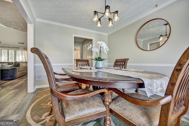 dining space featuring a textured ceiling, hardwood / wood-style flooring, an inviting chandelier, and ornamental molding