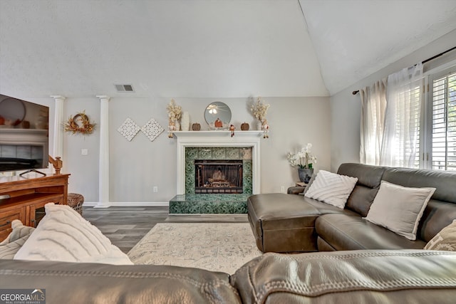 living room featuring ornate columns, vaulted ceiling, dark wood-type flooring, and a tiled fireplace