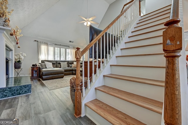 staircase with wood-type flooring, a textured ceiling, high vaulted ceiling, and ceiling fan