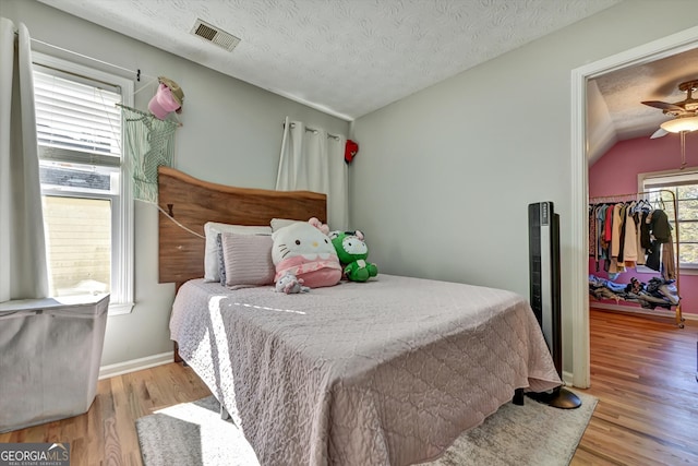 bedroom with light wood-type flooring, a textured ceiling, ceiling fan, a closet, and lofted ceiling