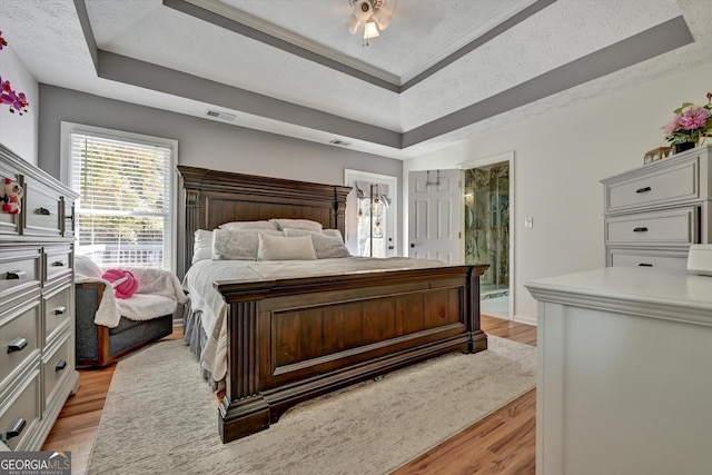 bedroom with a raised ceiling, ensuite bath, light hardwood / wood-style flooring, and a textured ceiling