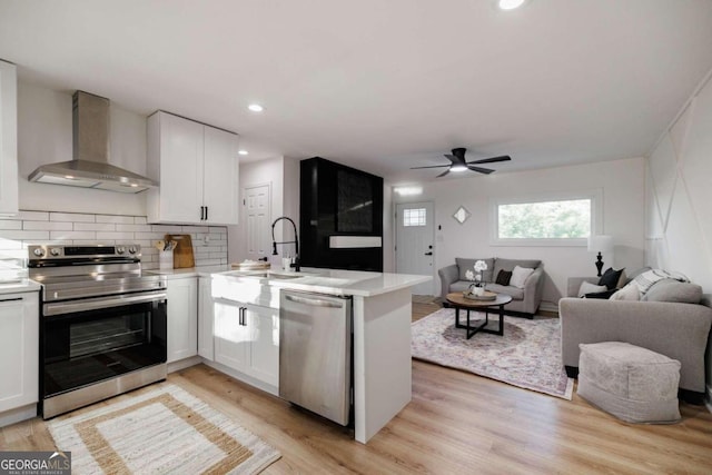 kitchen featuring kitchen peninsula, appliances with stainless steel finishes, light wood-type flooring, wall chimney exhaust hood, and white cabinets