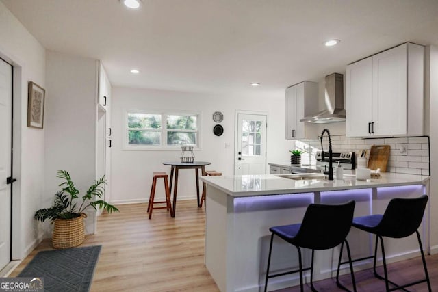 kitchen with decorative backsplash, kitchen peninsula, wall chimney range hood, white cabinets, and light hardwood / wood-style floors