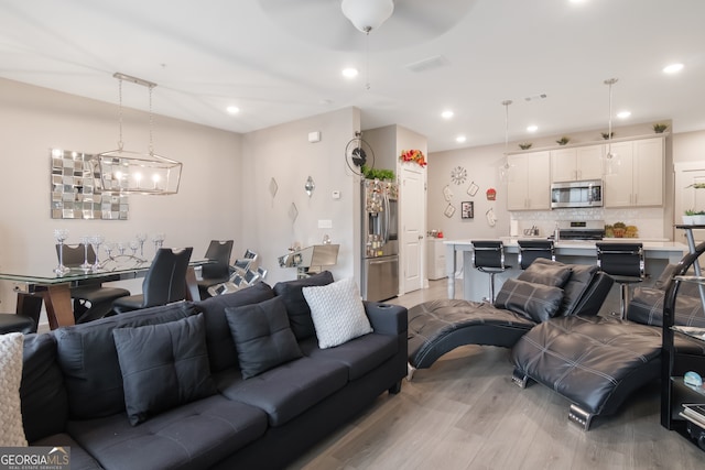 living room featuring ceiling fan with notable chandelier and light hardwood / wood-style floors