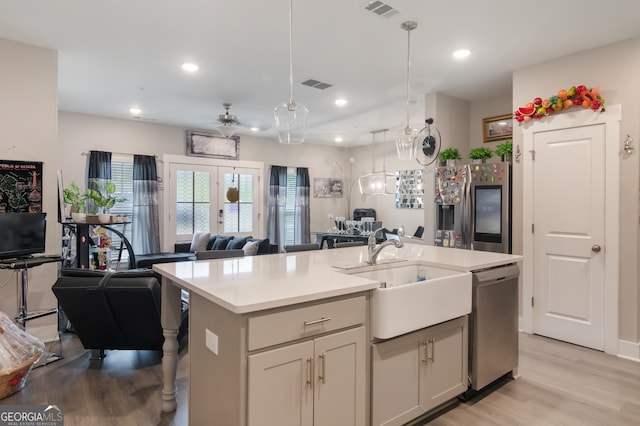 kitchen featuring a center island with sink, sink, hanging light fixtures, light hardwood / wood-style flooring, and stainless steel dishwasher