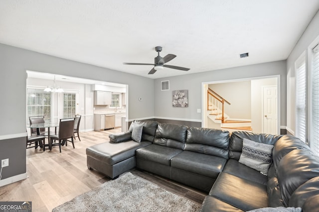 living room featuring ceiling fan with notable chandelier and light wood-type flooring