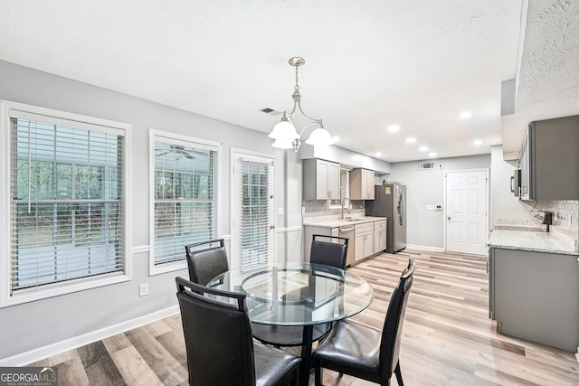 dining room with ceiling fan with notable chandelier, a textured ceiling, light wood-type flooring, and sink