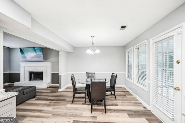 dining space with a notable chandelier, a fireplace, and light hardwood / wood-style flooring