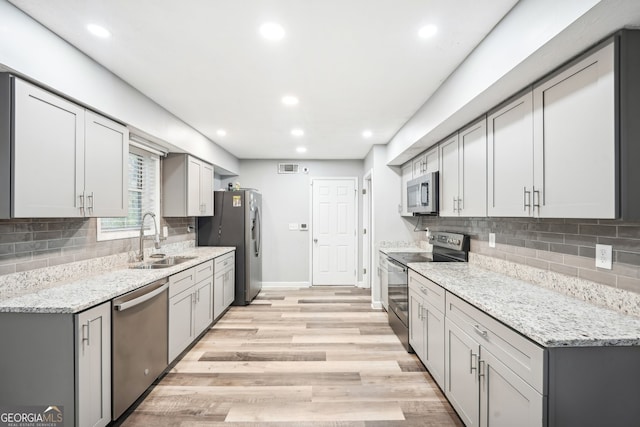 kitchen featuring gray cabinetry, sink, light stone counters, appliances with stainless steel finishes, and light wood-type flooring