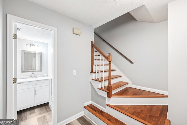 stairway with hardwood / wood-style floors, a textured ceiling, and sink