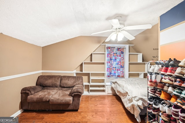 living area featuring a textured ceiling, ceiling fan, wood-type flooring, and vaulted ceiling