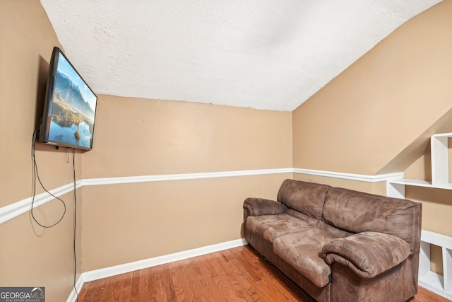 living area featuring lofted ceiling, wood-type flooring, and a textured ceiling