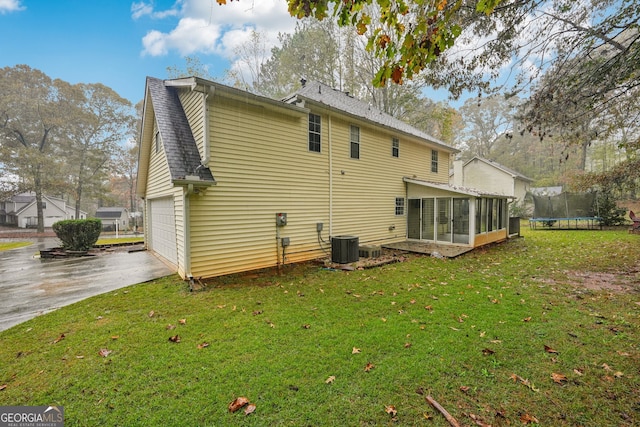 back of house with a lawn, a sunroom, a garage, and a trampoline