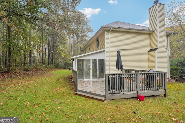 rear view of property featuring a wooden deck, a lawn, and a sunroom