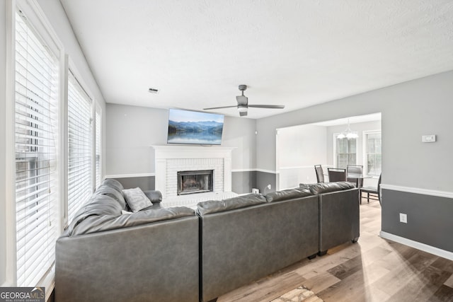 living room featuring hardwood / wood-style floors, ceiling fan with notable chandelier, a textured ceiling, and a brick fireplace