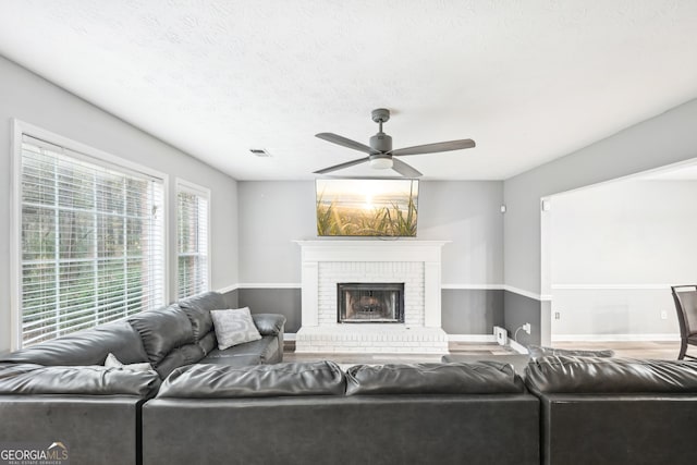 living room featuring ceiling fan, a textured ceiling, and a brick fireplace