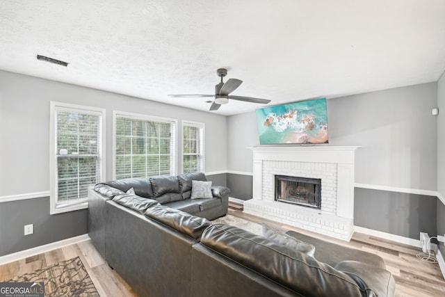 living room featuring a fireplace, a textured ceiling, light wood-type flooring, and ceiling fan