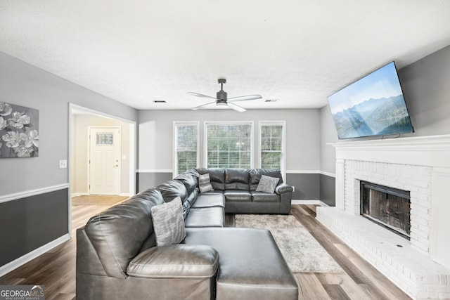 living room with a brick fireplace, ceiling fan, a textured ceiling, and hardwood / wood-style flooring