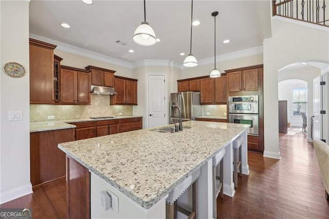 kitchen with light stone countertops, stainless steel appliances, sink, decorative light fixtures, and a center island with sink