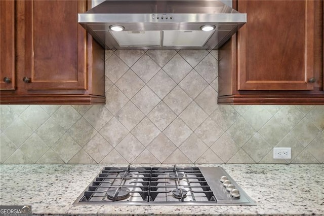 kitchen with light stone counters, wall chimney range hood, stainless steel gas cooktop, and tasteful backsplash