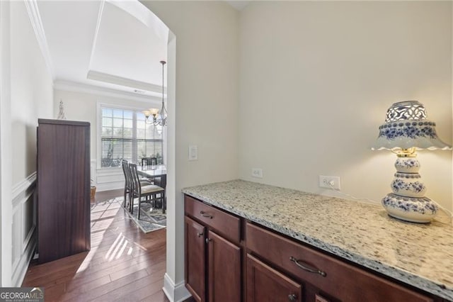 bar with an inviting chandelier, light stone countertops, ornamental molding, a tray ceiling, and light hardwood / wood-style floors