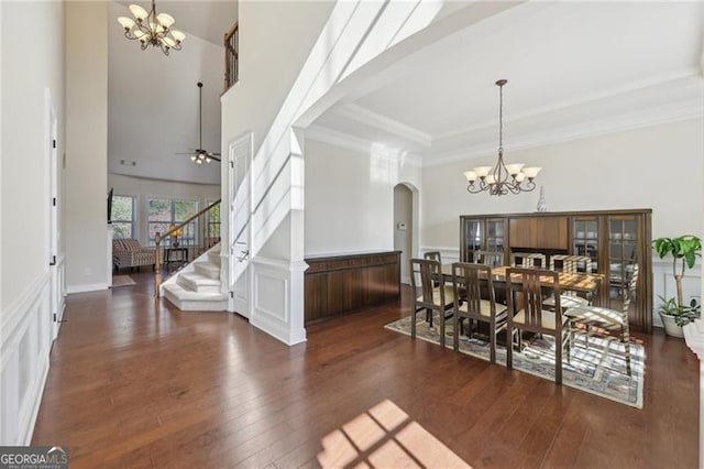 dining space with crown molding, a towering ceiling, dark wood-type flooring, and ceiling fan with notable chandelier