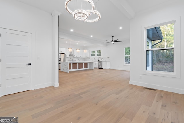 unfurnished living room featuring ceiling fan with notable chandelier, beamed ceiling, and light wood-type flooring