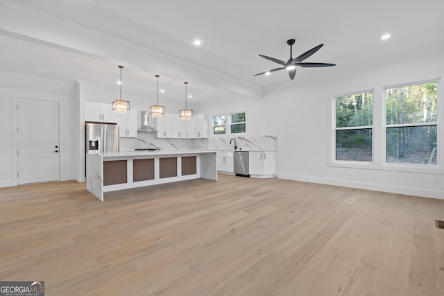 kitchen featuring a center island, appliances with stainless steel finishes, white cabinets, pendant lighting, and wall chimney range hood