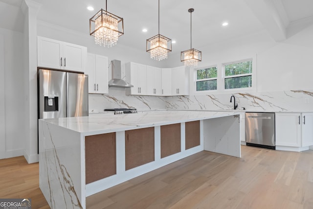 kitchen featuring appliances with stainless steel finishes, light stone countertops, a kitchen island, wall chimney exhaust hood, and white cabinets