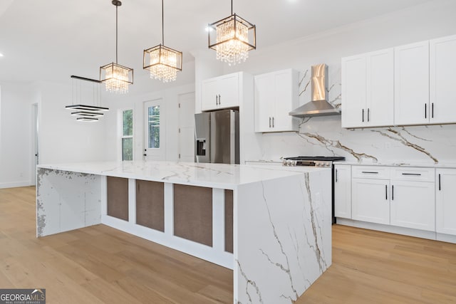 kitchen featuring decorative light fixtures, appliances with stainless steel finishes, wall chimney range hood, and white cabinetry