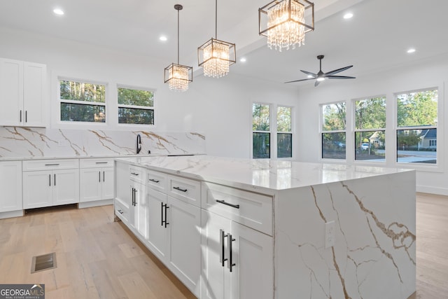 kitchen with backsplash, light stone counters, white cabinetry, and pendant lighting