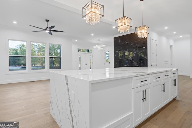 kitchen with ceiling fan with notable chandelier, white cabinets, a kitchen island, decorative light fixtures, and light stone counters