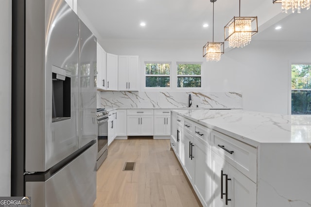 kitchen featuring decorative light fixtures, white cabinets, light stone countertops, and appliances with stainless steel finishes