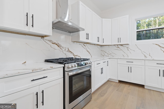 kitchen with backsplash, wall chimney exhaust hood, stainless steel gas stove, and white cabinetry