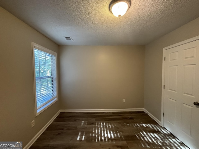 spare room with a textured ceiling and dark hardwood / wood-style flooring