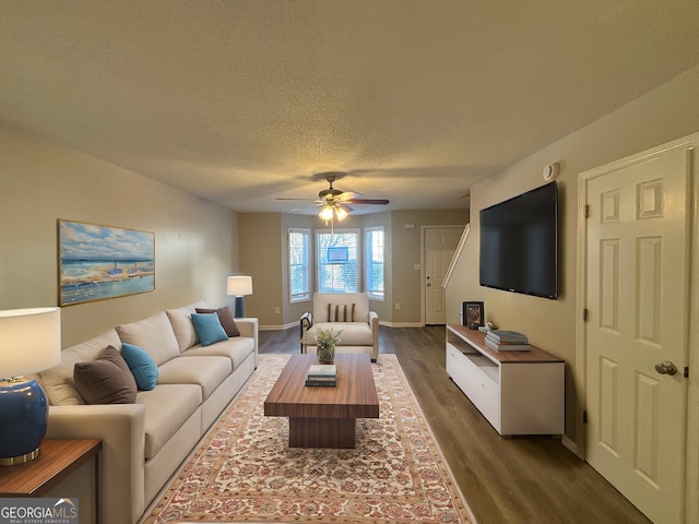 living room with a textured ceiling, ceiling fan, and dark wood-type flooring