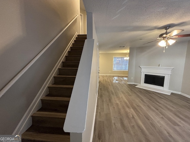 staircase with hardwood / wood-style floors, a textured ceiling, and ceiling fan