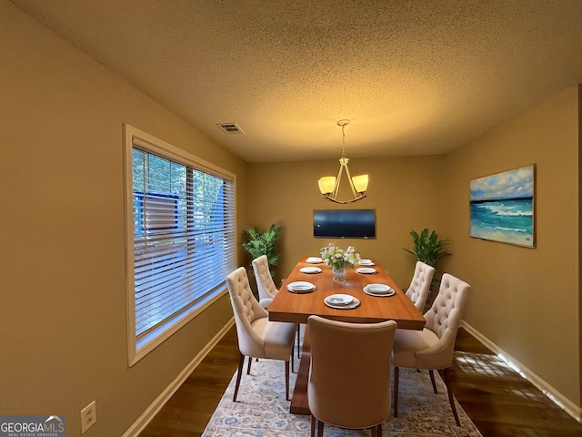 dining area featuring an inviting chandelier, a textured ceiling, and dark hardwood / wood-style floors