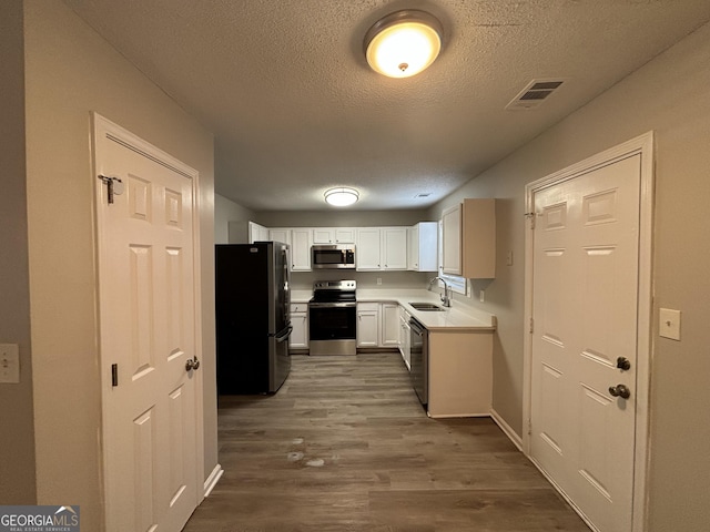 kitchen with appliances with stainless steel finishes, dark hardwood / wood-style flooring, a textured ceiling, white cabinetry, and sink