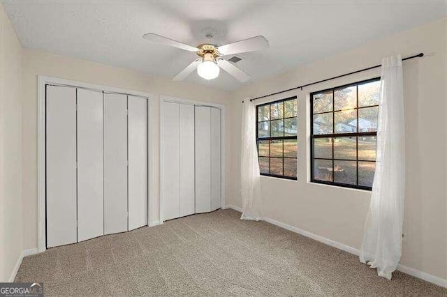 unfurnished bedroom with light carpet, ceiling fan, and multiple closets