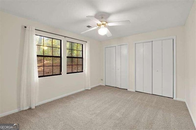 unfurnished bedroom with ceiling fan, light colored carpet, and two closets