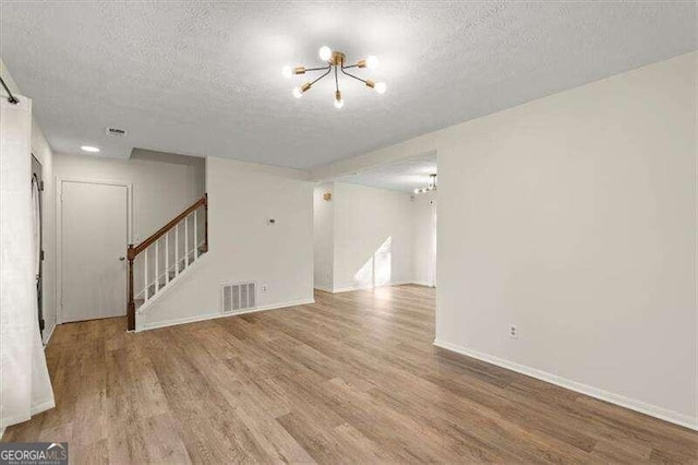 unfurnished living room featuring a textured ceiling, light hardwood / wood-style floors, and a notable chandelier