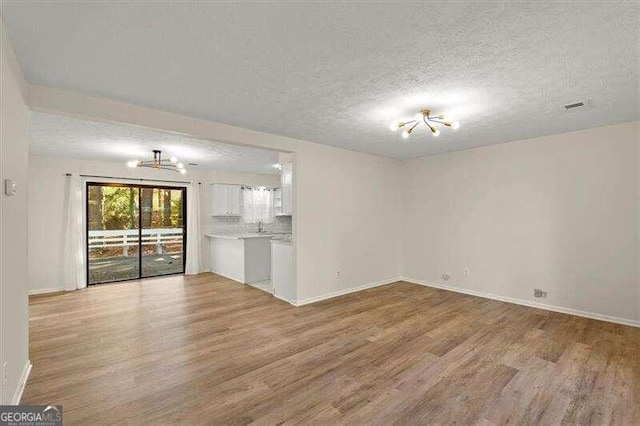 unfurnished living room with light hardwood / wood-style floors, sink, and a textured ceiling