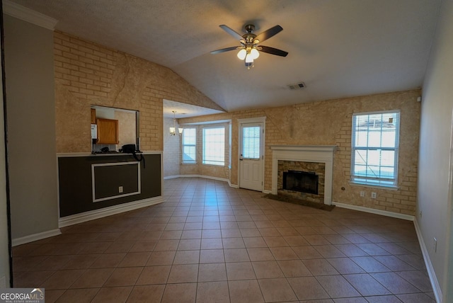 unfurnished living room with brick wall, ceiling fan with notable chandelier, vaulted ceiling, light tile patterned floors, and a fireplace