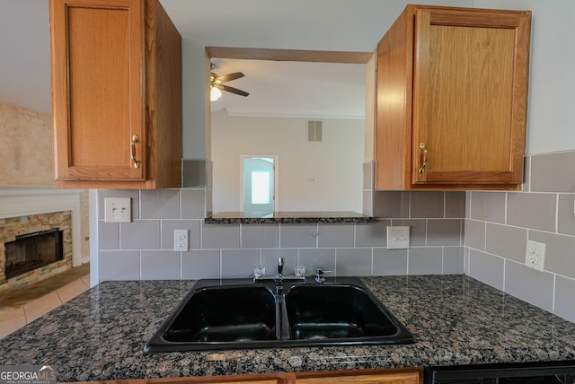 kitchen featuring tasteful backsplash, a stone fireplace, ceiling fan, and sink