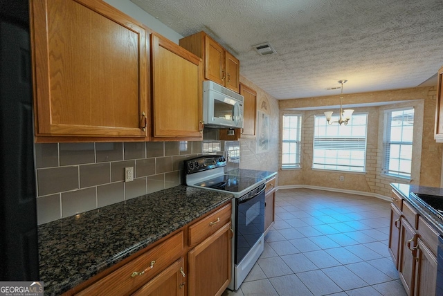 kitchen with white appliances, dark stone counters, an inviting chandelier, hanging light fixtures, and light tile patterned floors