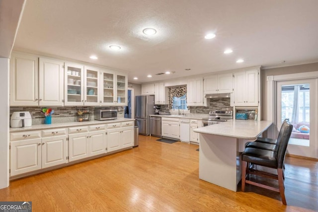 kitchen featuring a breakfast bar, backsplash, appliances with stainless steel finishes, light hardwood / wood-style floors, and white cabinetry