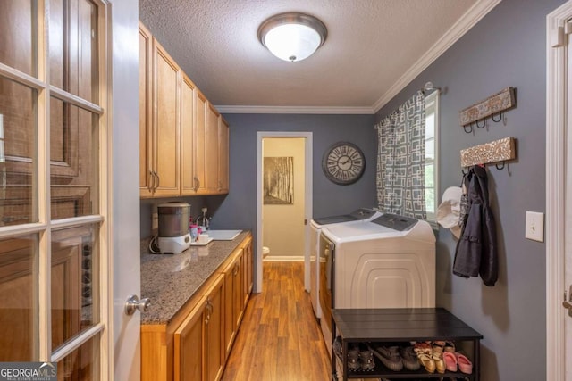 washroom featuring ornamental molding, a textured ceiling, sink, washing machine and clothes dryer, and light hardwood / wood-style floors